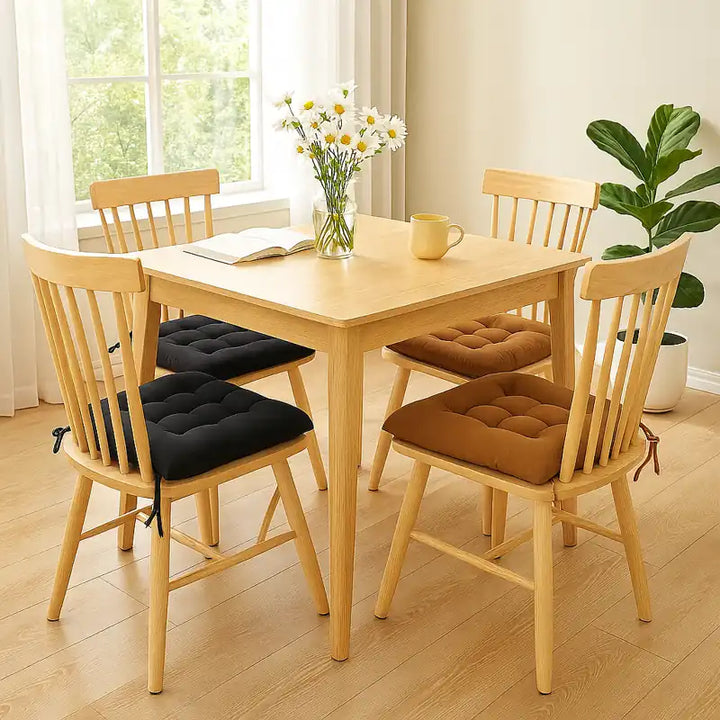 Salle à manger lumineuse et élégante, table en bois clair entourée de chaises décorées de coussins rembourrés carrés en coton marron et noir.