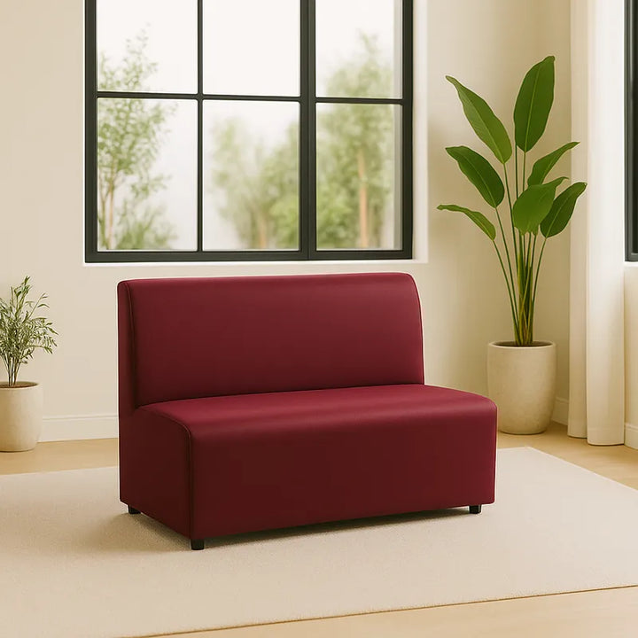 Banquette recouverte d’une housse en simili cuir bordeaux, placée dans un salon moderne et minimaliste avec un grand vitrage noir, un tapis beige et des plantes vertes. L’ambiance est lumineuse, élégante et équilibrée.