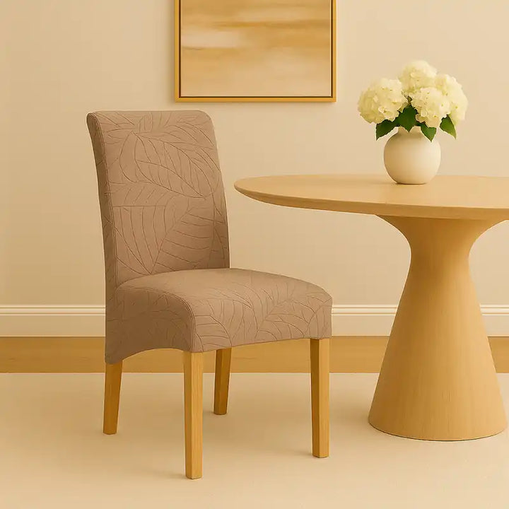 Salle à manger moderne et élégante aux tons beige et crème, avec une table ovale beige et une chaise recouverte d’une housse en jacquard effet floral beige clair. Le décor comprend un mur beige orné d’un tableau minimaliste, un éclairage doux et une ambiance chaleureuse et raffinée.