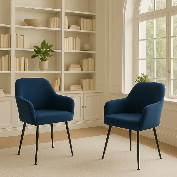 Deux chaises modernes recouvertes de housses en velours bleu marine avec accoudoirs sont placées sur un tapis beige, devant une grande bibliothèque blanche ornée de livres.