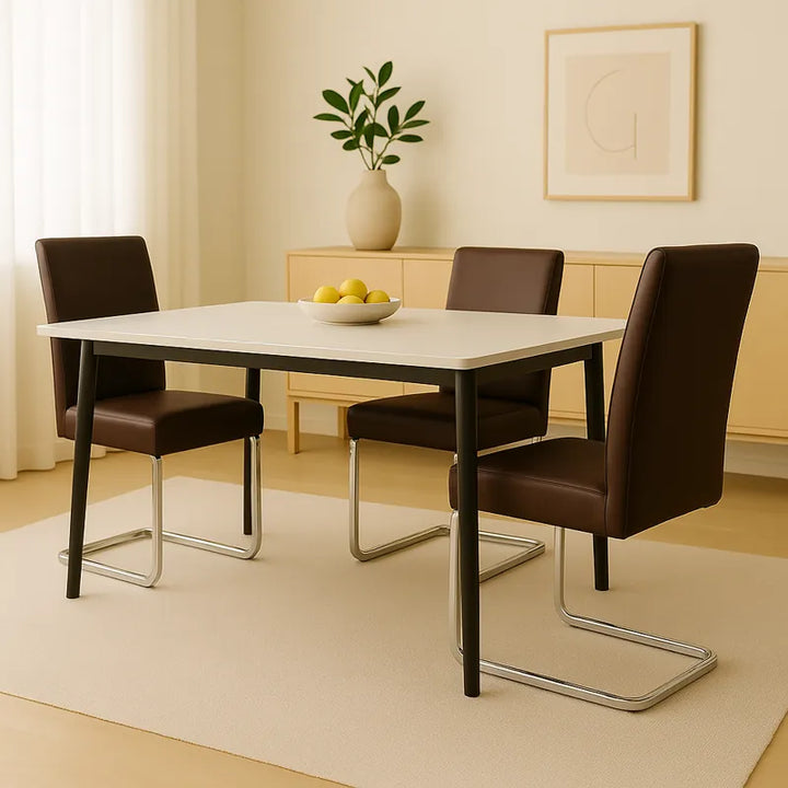 Salle à manger moderne et lumineuse avec trois chaises en simili cuir marron à piètement métallique chromé, disposées autour d’une table rectangulaire au plateau clair. Le décor minimaliste comprend un buffet en bois clair, une plante verte dans un vase beige et un tableau mural épuré, créant une ambiance élégante et raffinée.