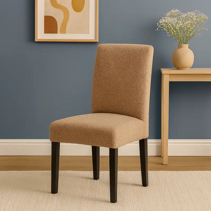 Chaise recouverte d’une housse en polaire beige, placée dans un salon moderne et lumineux aux tons beige et bleu. À l’arrière-plan, un tableau abstrait et un petit meuble en bois clair orné d’un vase en céramique beige contenant des fleurs blanches. L’ensemble crée une atmosphère douce, élégante et chaleureuse.