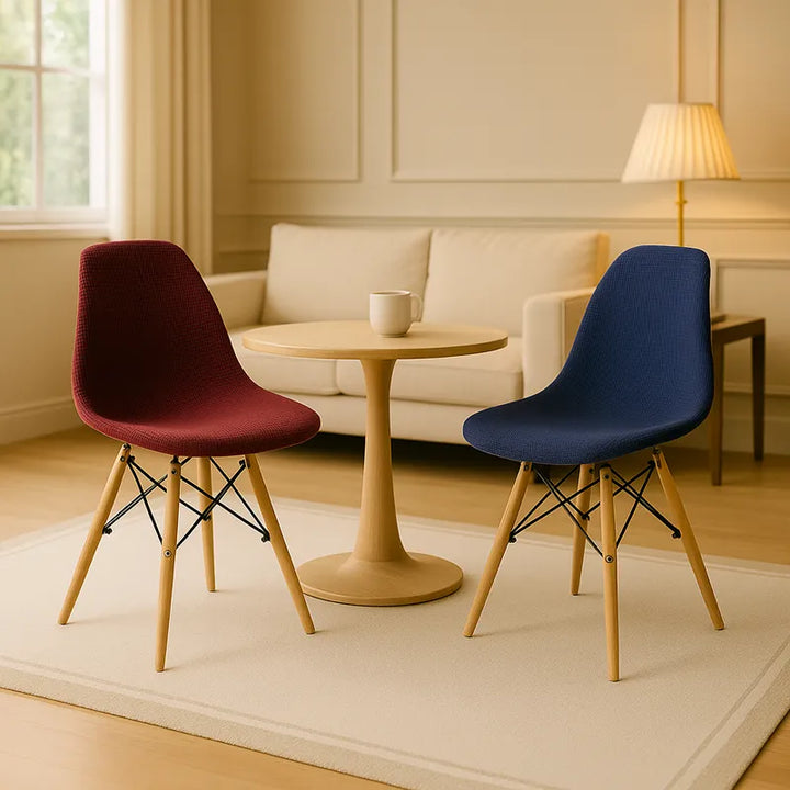 Deux chaises scandinaves élégantes, l’une bordeaux et l’autre bleue, entourent une table ronde en bois clair dans un salon lumineux et raffiné. Un canapé beige, une lampe dorée et un grand tapis clair complètent la scène, baignée de lumière naturelle provenant d’une grande fenêtre. L’ensemble crée une atmosphère moderne, chic et harmonieuse.