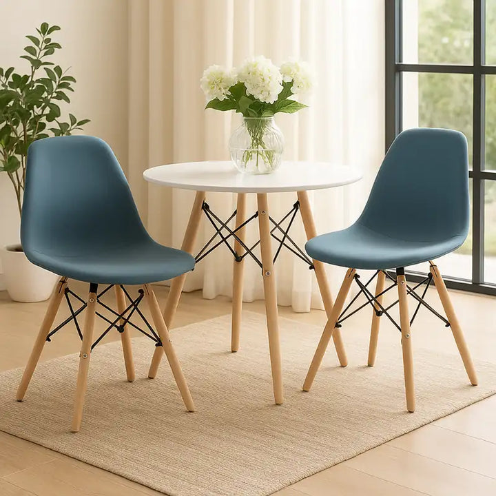 Deux chaises scandinaves bleues avec pieds en bois clair, disposées autour d’une table ronde blanche.