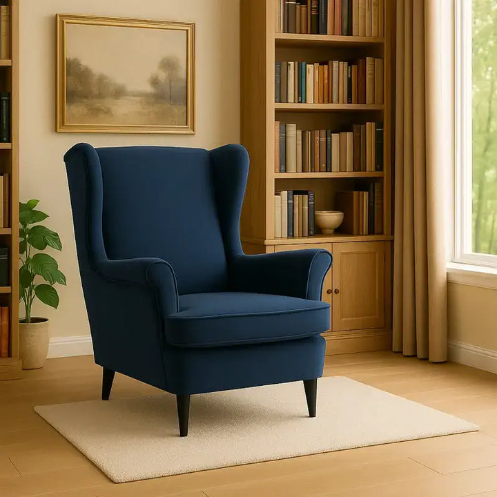 Fauteuil à oreilles bleu en velours dans une bibliothèque lumineuse.