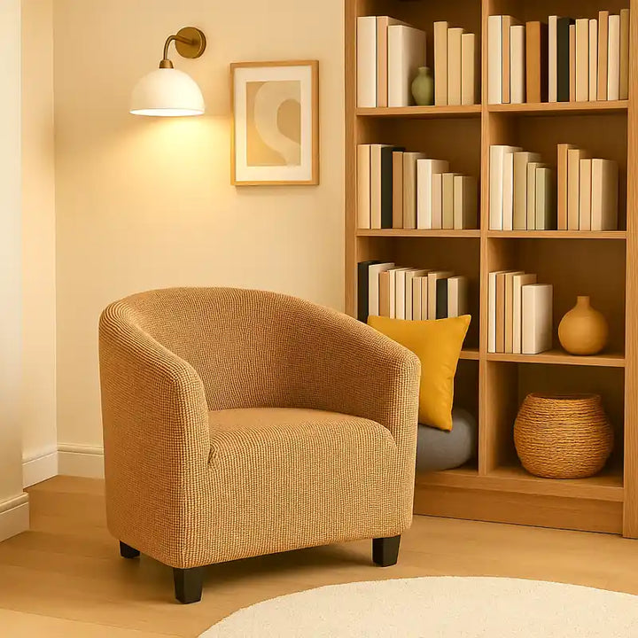 Fauteuil en jacquard beige disposé dans une bibliothèque moderne et luxueuse, entouré d’étagères remplies de livres et de lampes design dorées diffusant une lumière douce. L’ambiance est chaleureuse et élégante, avec des coussins colorés et un fond beige clair qui met en valeur la texture du tissu jacquard.
