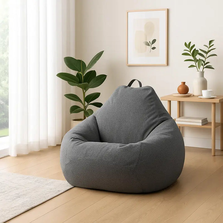 Pièce de repos moderne et lumineuse avec un pouf gris recouvert d’une housse élégante en tissu imperméable. L’espace est baigné de lumière naturelle provenant de grandes baies vitrées, décoré avec des plantes vertes et un tapis doux, créant une ambiance paisible et raffinée.