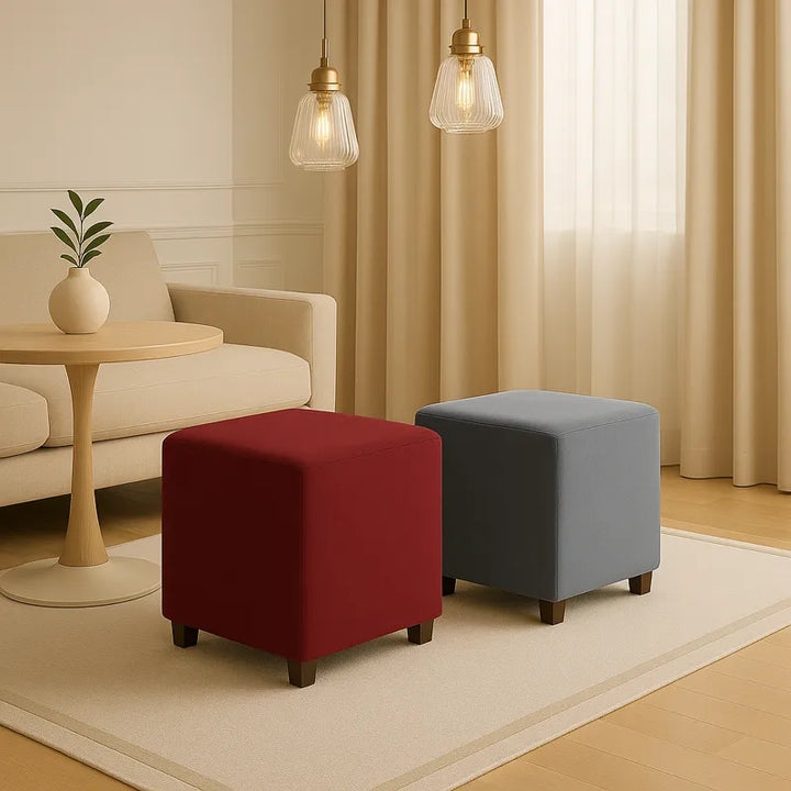 Deux poufs carrés en velours, l’un bordeaux et l’autre gris, sont disposés sur un tapis beige dans un salon élégant et lumineux.