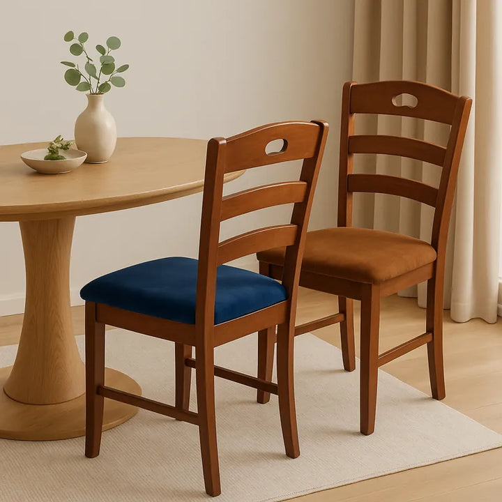 Deux chaises en bois avec housses de siège en velours, l’une bleue et l’autre marron, disposées autour d’une table ovale en bois clair dans une salle à manger lumineuse et sobre, décorée avec des tons beiges et naturels pour une ambiance élégante et chaleureuse.