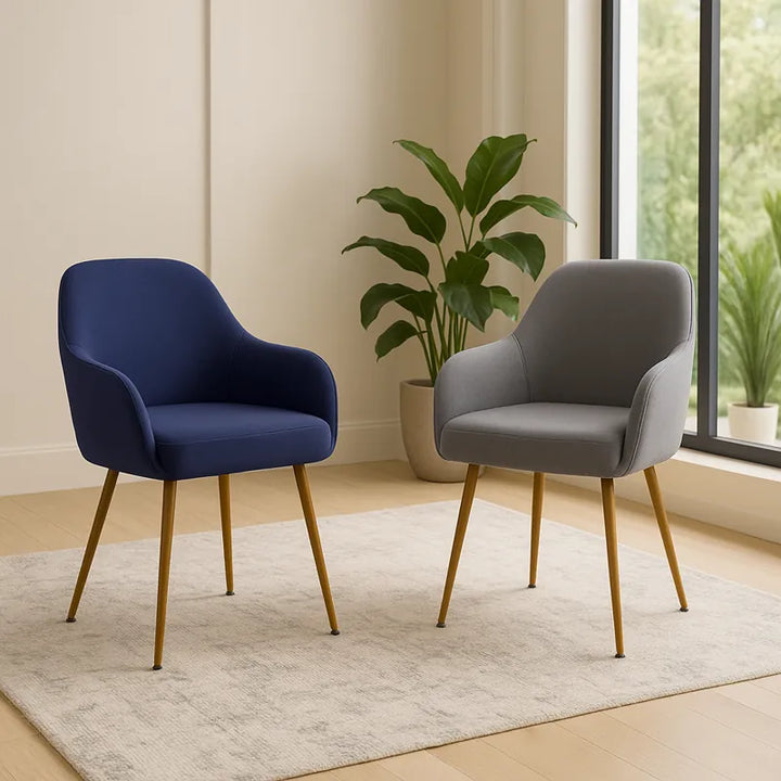 Deux chaises modernes avec accoudoirs, l’une bleue et l’autre grise, mises en valeur dans un salon élégant et lumineux aux tons beiges, avec une grande baie vitrée, des plantes vertes et une ambiance sobre et luxueuse.